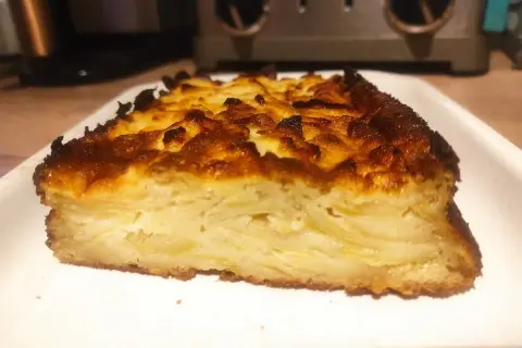 Tranche épaisse d'un délicieux cake aux pommes, avec une croûte dorée et caramélisée.