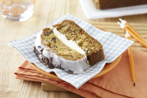 Tranche de carrot cake moelleux avec glaçage blanc et copeaux de chocolat. Un délice à savourer !