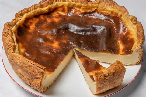 Un flan pâtissier doré, avec une croûte croustillante et une garniture crémeuse, une part coupée révèle sa texture onctueuse.