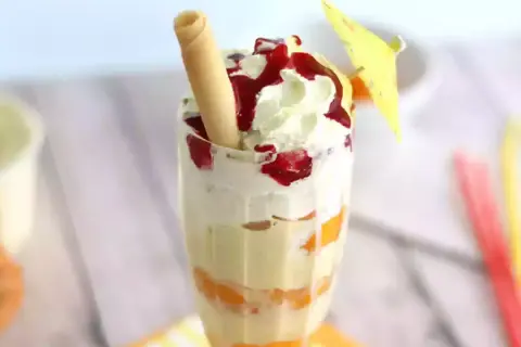Un déliceux pêche Melba, avec des couches de fruits, de crème fouettée et de coulis de fruits rouges, garni d'une gaufrette et d'un petit parasol.