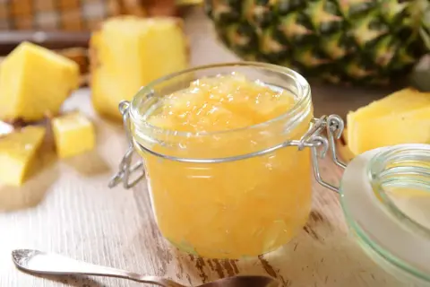 Un pot de confiture d'ananas maison, entouré de morceaux d'ananas frais et d'une cuillère.