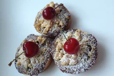 Trois petites tartelettes aux cerises, saupoudrées de sucre glace et ornées d'une cerise fraîche sur le dessus.