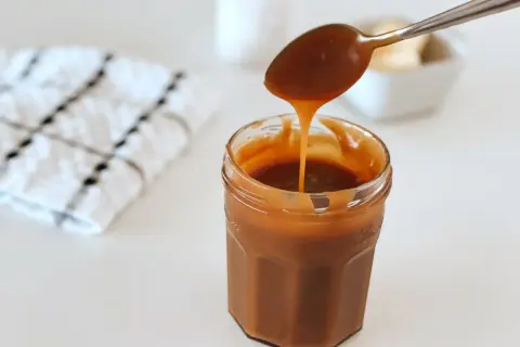 Une cuillère verse un caramel beurre salé onctueux dans un pot en verre.