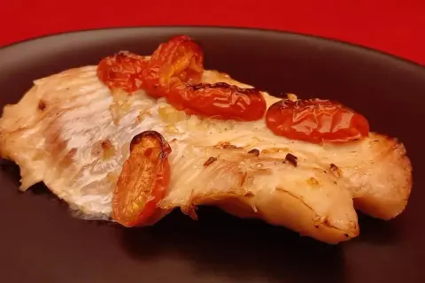 Un délicieux filet de dorade au four, garni de tomates cerises rôties, sur une assiette noire.