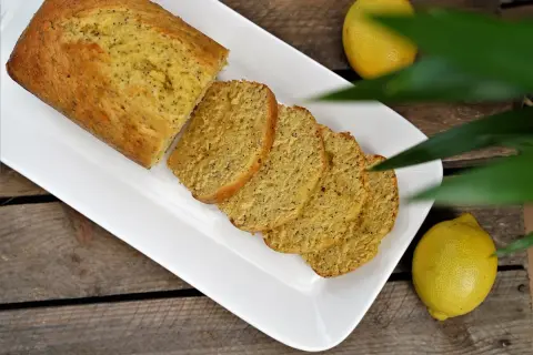 Un délicieux cake citron pavot, coupé en tranches, servi sur une assiette blanche, avec des citrons frais à côté.