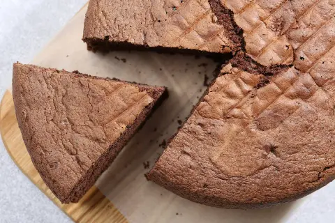 Un gâteau chocolat Pierre Hermé, moelleux et aérien, avec une part coupée sur une planche en bois.