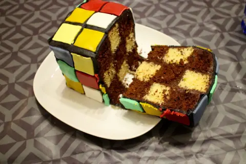 Un gâteau Rubik's cube, coupé en deux, révèle un intérieur marbré chocolat et vanille. Les couleurs vives du glaçage rappellent le célèbre casse-tête.