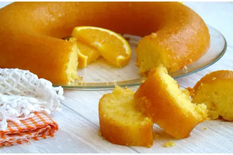 Un délicieux cake à l'orange, avec des tranches d'orange fraîche, servi sur une assiette en verre. Une part est déjà coupée.