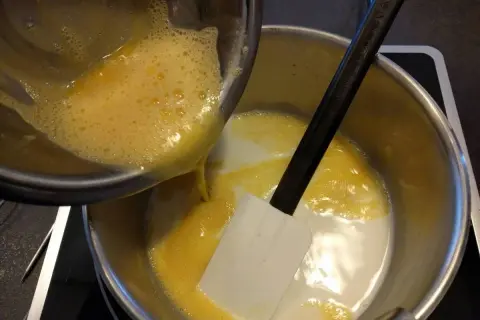 Préparation d'une recette crémeux vanille Michalak : on verse un mélange d'œufs battus dans une casserole contenant du lait et une spatule.