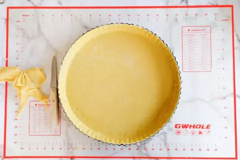 Pâte brisée salée prête à être garnie dans un moule à tarte. Des chutes de pâte et un couteau sont à côté.