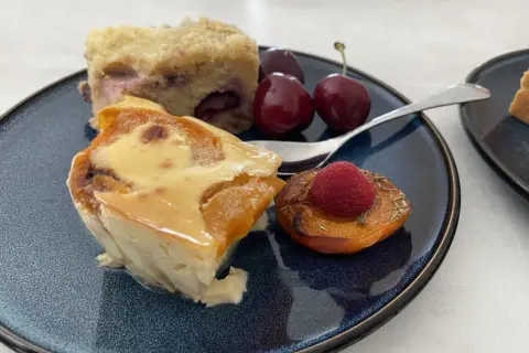 Un délice de clafoutis abricot, servi avec des cerises et une framboise sur une pêche rôtie.