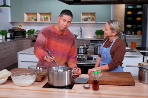 Un homme et une femme préparent un plat dans une cuisine. Le bouillon de poulet mijote dans une grande casserole.