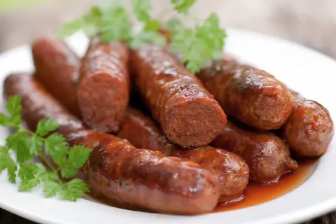 Assiette de merguez au four, dorées et juteuses, garnie de persil frais. Un délice prêt à être dégusté.