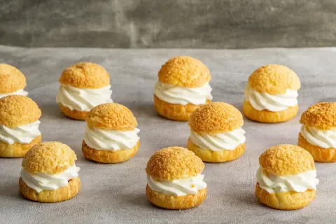 Douze petits choux garnis de crème fouettée, prêts à être dégustés. Ces délices de pâte à choux sont parfaits pour un goûter.