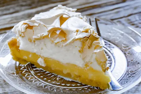 Une part de tarte au citron meringuée, avec sa crème jaune acidulée et sa meringue dorée, prête à être dégustée.