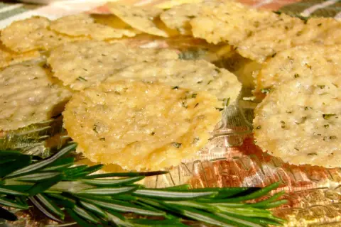 Délicieuses tuiles parmesan poêle, croustillantes et dorées, parsemées d'herbes. Une branche de romarin frais ajoute une touche aromatique.