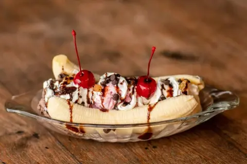 Un déliceux banana split garni de crème fouettée, de cerises et de sauce au chocolat, prêt à être dégusté.