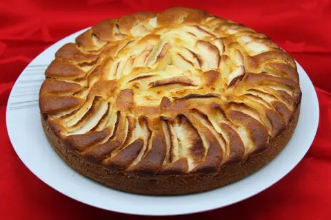 Un délicieux gâteau yaourt pomme, doré et appétissant, orné de fines lamelles de pommes disposées en rosace sur le dessus.