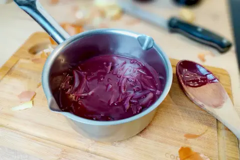 Sauce porto facile mijotant dans une casserole, avec des oignons rouges et une cuillère en bois.