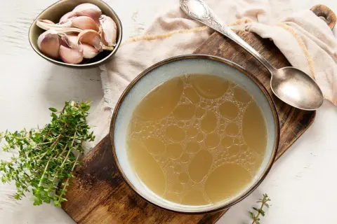 Un bol de bouillon de volaille doré, avec de l'ail et du thym. Idéal pour savoir comment faire un bouillon de volaille savoureux.