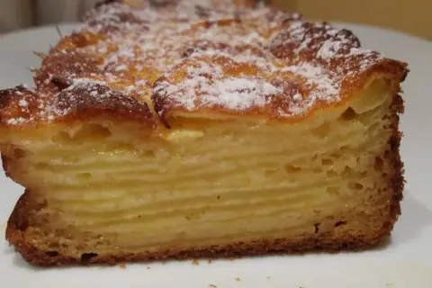 Tranche d'un gâteau aux pommes, feuilleté et doré, saupoudré de sucre glace. Un délice invisible aux pommes.