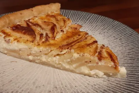 Une part de tarte aux pommes à l'ancienne, avec sa garniture crémeuse et ses pommes caramélisées, sur une assiette décorée.