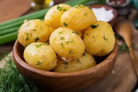 Pommes de terre à l'eau, tendres et parsemées d'aneth frais, dans un bol en bois. Un plat simple et savoureux.