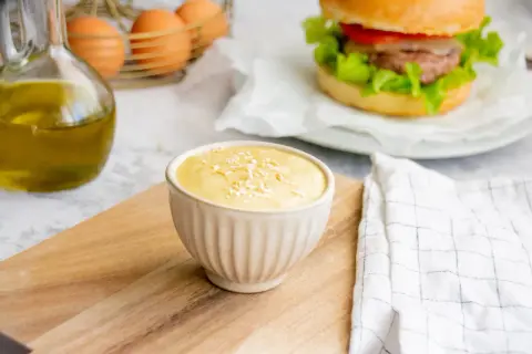 Sauce burger maison crémeuse, garnie de flocons, prête à accompagner un burger savoureux. Huile d'olive et œufs en arrière-plan.