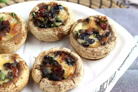 Champignons farcis au four, garniture aux olives noires et tomates séchées, fromage fondant. Une recette simple et savoureuse.