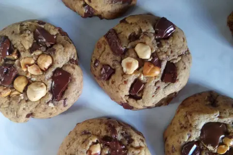 Gros plan sur des cookies américains faits maison, débordant de pépites de chocolat noir et de noisettes. Parfaits pour une recette de cookies américain gourmande.