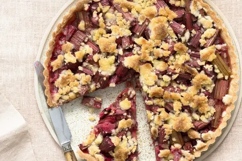 Tarte crumble à la rhubarbe, une délicieuse recette avec rhubarbe, garnie de morceaux de fruits rouges et d'une pâte croustillante.