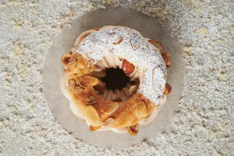 Un délicieux Paris-Brest, saupoudré de sucre glace et garni d'amandes grillées, attend d'être dégusté.