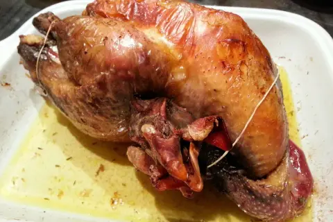 Une pintade au four, dorée et juteuse, repose dans un plat blanc, baignant dans son jus savoureux.