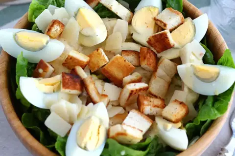 Salade César appétissante dans un bol en bois, garnie d'œufs durs, de croûtons dorés et d'une onctueuse sauce César.
