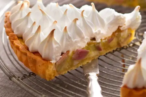 Une part de tarte rhubarbe meringuée, avec sa croûte dorée et sa garniture acidulée, surmontée d'une meringue légère et aérienne.