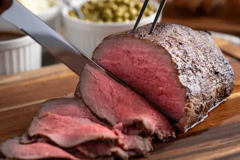 Un délicieux rôti de boeuf, coupé en fines tranches rosées, est prêt à être servi avec des accompagnements.
