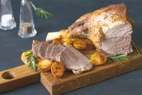 Un gigot de 7 heures, tendre et savoureux, servi avec des pommes de terre rôties et du romarin sur une planche en bois.