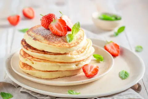 Pile de pancakes moelleux, parsemés de sucre glace et ornés de fraises fraîches et de menthe. Un délice digne des pancakes Cyril Lignac.