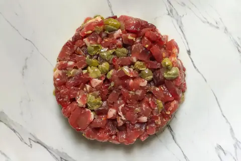Un délicieux tartare de bœuf gastronomique, préparé avec soin et garni de câpres, prêt à être dégusté.