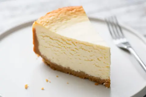 Une part de gâteau au fromage blanc onctueux, digne d'un gâteau au fromage blanc Cyril Lignac, sur une assiette blanche avec une fourchette.