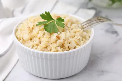 Un bol de boulgour cuit, garni d'une feuille de persil, prêt à être dégusté. La cuisson du boulgour est simple et rapide.