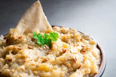 Un bol de le vrai caviar d'aubergine, garni de persil frais et de graines de sésame, avec un morceau de pain pita.