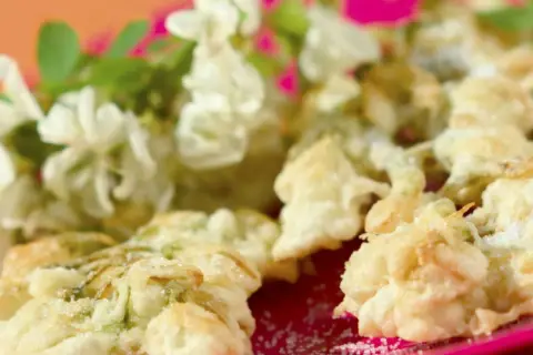 Délicieux beignets de fleur d'acacia à la poêle, saupoudrés de sucre, avec des fleurs fraîches en arrière-plan.