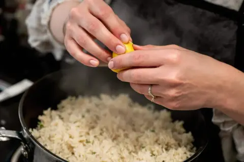 Cuisson du riz rouge : une main presse un quartier de citron sur le riz fumant dans une casserole.