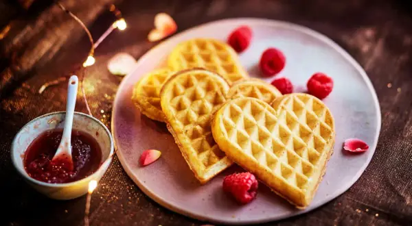 Gaufres en forme de cœur, parfaites pour une recette gaufre moelleuse, servies avec de la confiture de framboise et des fruits rouges.