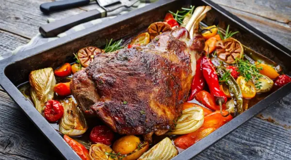 Un plat appétissant d'épaule d'agneau au four, rôti à la perfection avec des légumes colorés comme des poivrons, des tomates et de l'ail.