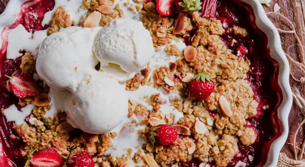 Un délicieux crumble rhubarbe fraise, garni de boules de glace à la vanille fondante et d'amandes effilées.
