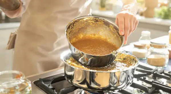 Une personne verse un liquide doré, du caramel à sec, d'une casserole à une autre sur une cuisinière.