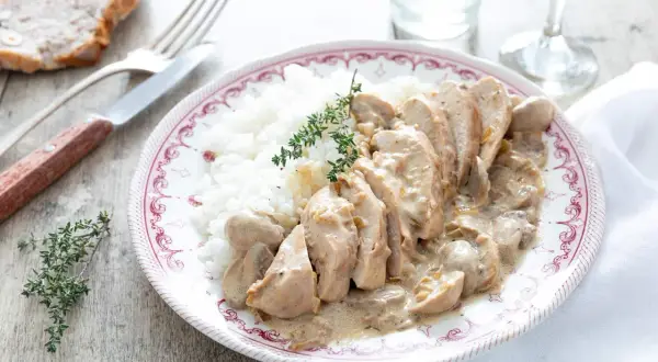 Une assiette de riz blanc avec des tranches de poulet nappées d'une sauce onctueuse au poulet crème champignon, garnie de thym frais.