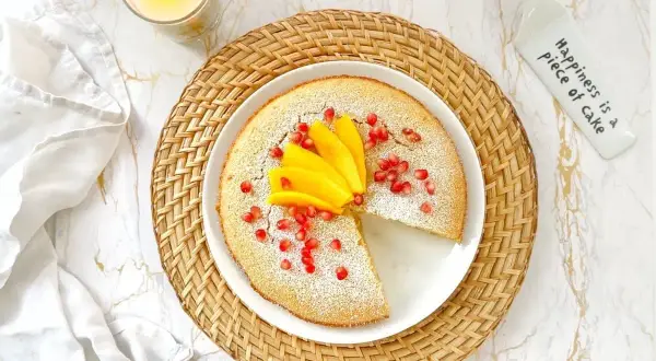 Un délicieux flan coco saupoudré de sucre glace, garni de mangue et de grenades. Une part manque, invitant à la gourmandise.